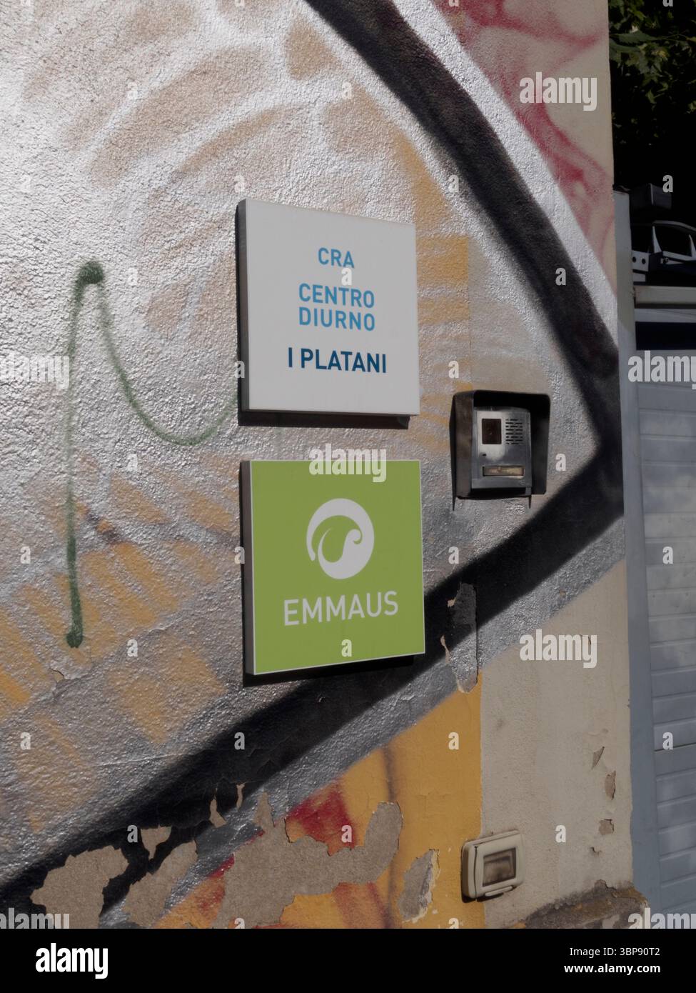 Bologna, Italia 3 luglio 2025 cartello stradale per Emmaus e Centro Diurno i Platani, marcatura graffiti rivestito muro urbano a Bologna, in mostra Grity Ital Foto Stock