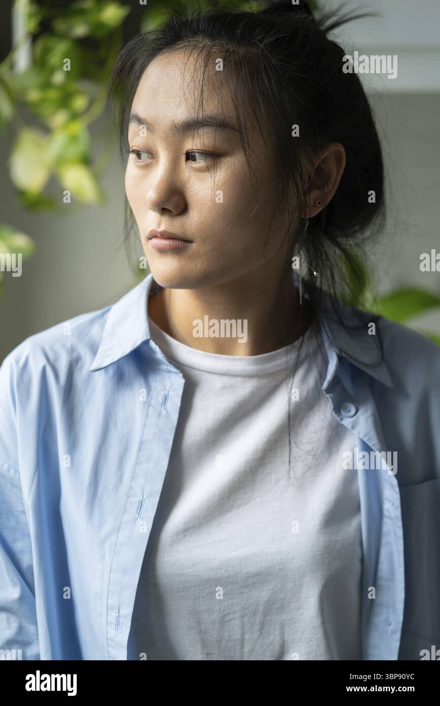 Infelice triste giovane donna asiatica che guarda da parte, sente disperazione, depressa donna pessimista a casa in piedi a casa pensando alla vita quotidiana pro Foto Stock