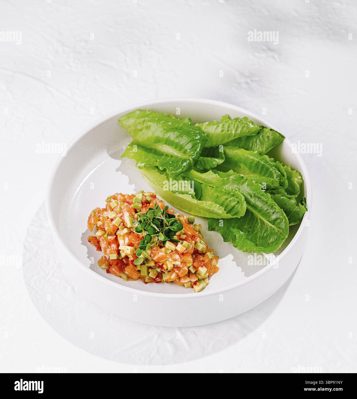 Cibo, tartare di salmone servita con avocado, erbe aromatiche e lattuga su piatto bianco su sfondo bianco Foto Stock
