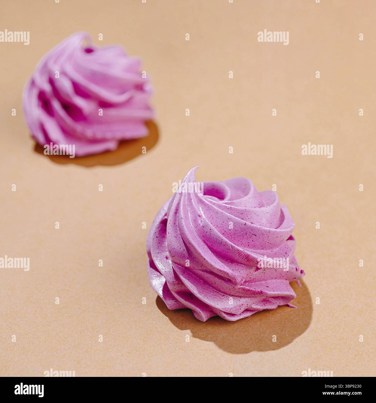 Cibo, due delicati vortici di meringa rosa posizionati artisticamente su uno sfondo caldo color pesca Foto Stock