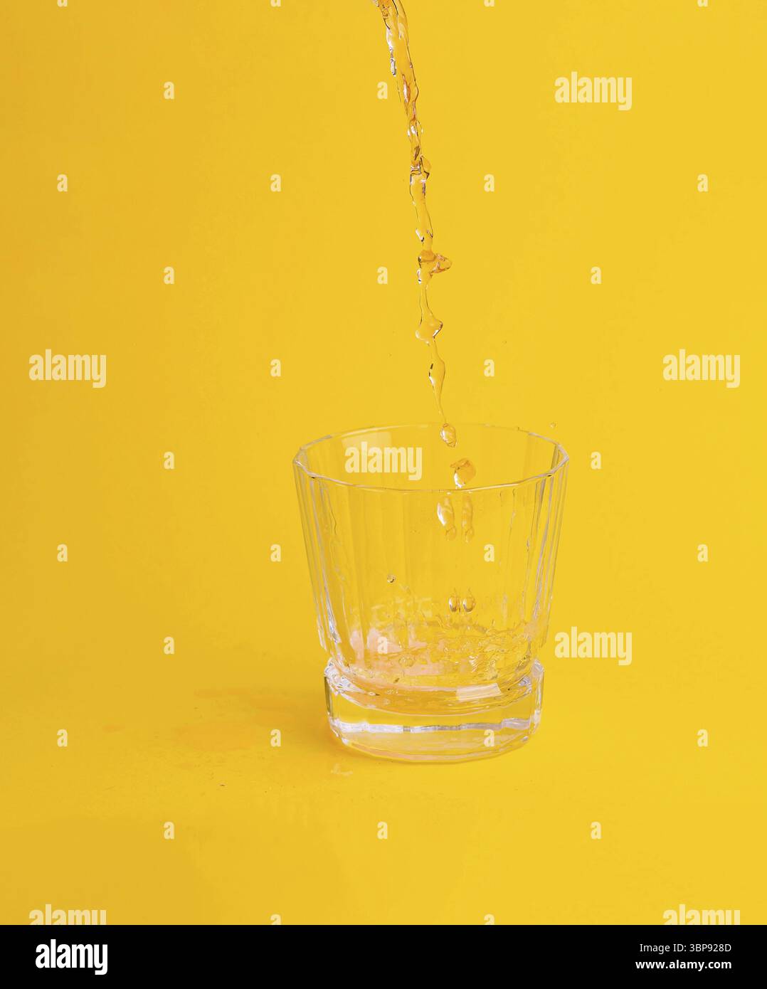 Cibo, flusso d'acqua versato in un bicchiere su sfondo giallo creando bolle Foto Stock