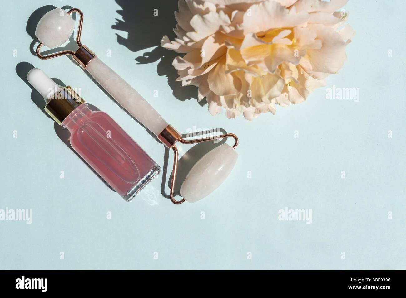 Flacone trasparente con siero di bellezza, acido ialuronico e acqua di rosa su sfondo blu con rullo al quarzo massaggiante. Lussuosa auto per il viso e il corpo della casa Foto Stock