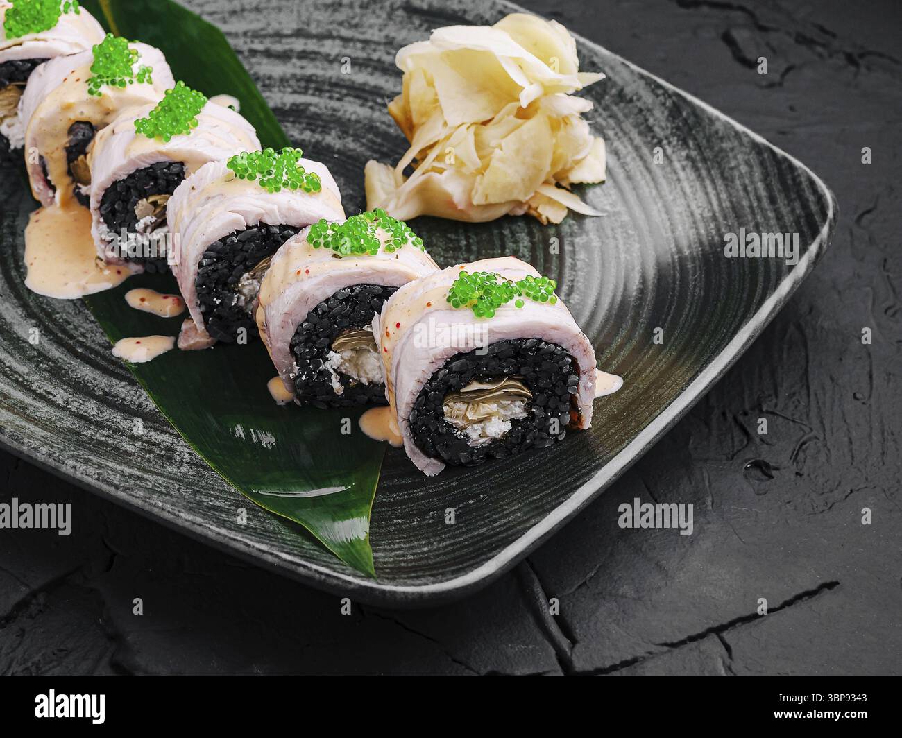 Cibo, Un sushi roll ben organizzato fatto con riso nero, ricoperto di caviale verde e accompagnato da zenzero sottaceto. Il piatto presenta piatti culinari Foto Stock