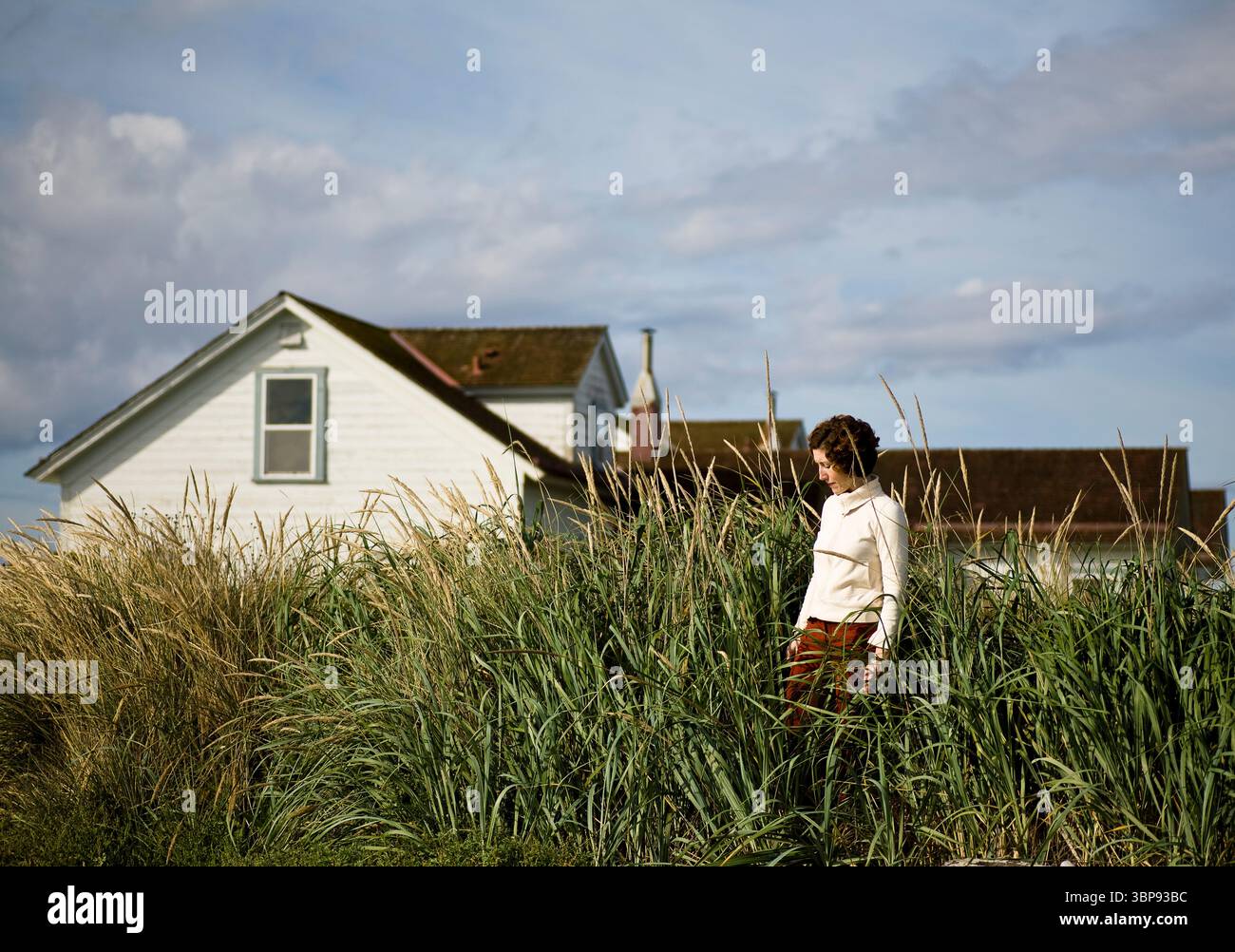 Una giovane donna guarda in basso nell'erba lunga di fronte agli edifici del faro. Foto Stock