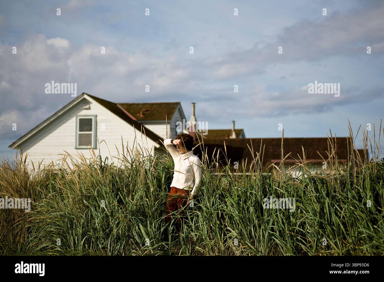 Una giovane donna protegge gli occhi contro il sole che tramonta davanti agli edifici del faro. Foto Stock