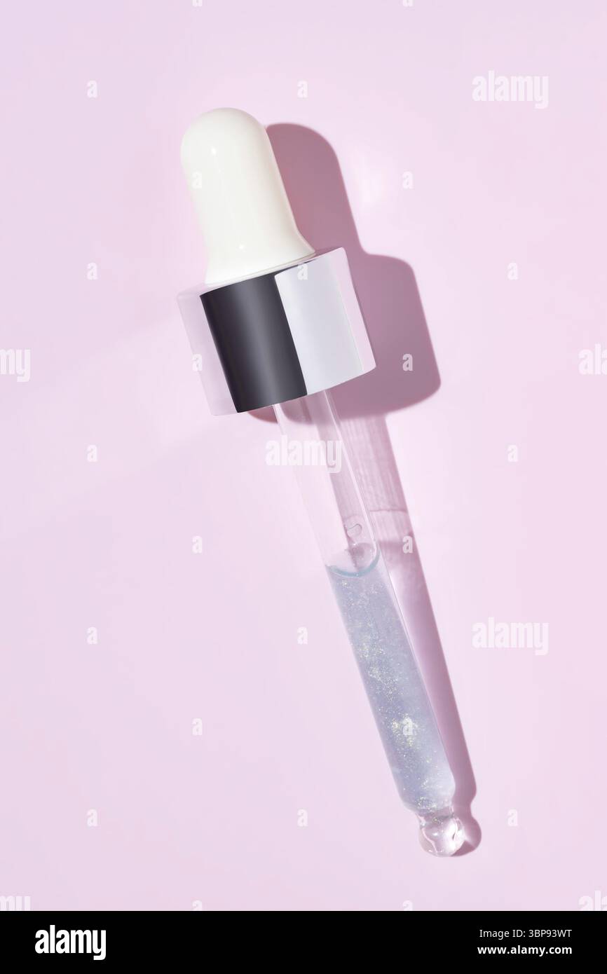 Primo piano della pipetta con il versamento di siero liquido e ombre su sfondo rosa. Cosmetici alla moda con ombre dure Foto Stock