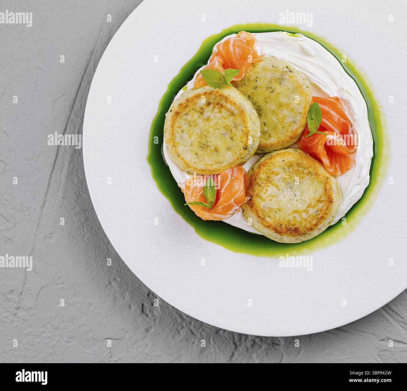 Cibo, vista dall'alto di delicate torte di pesce servite con una vivace salsa alle erbe e guarnite con pezzi di salmone Foto Stock