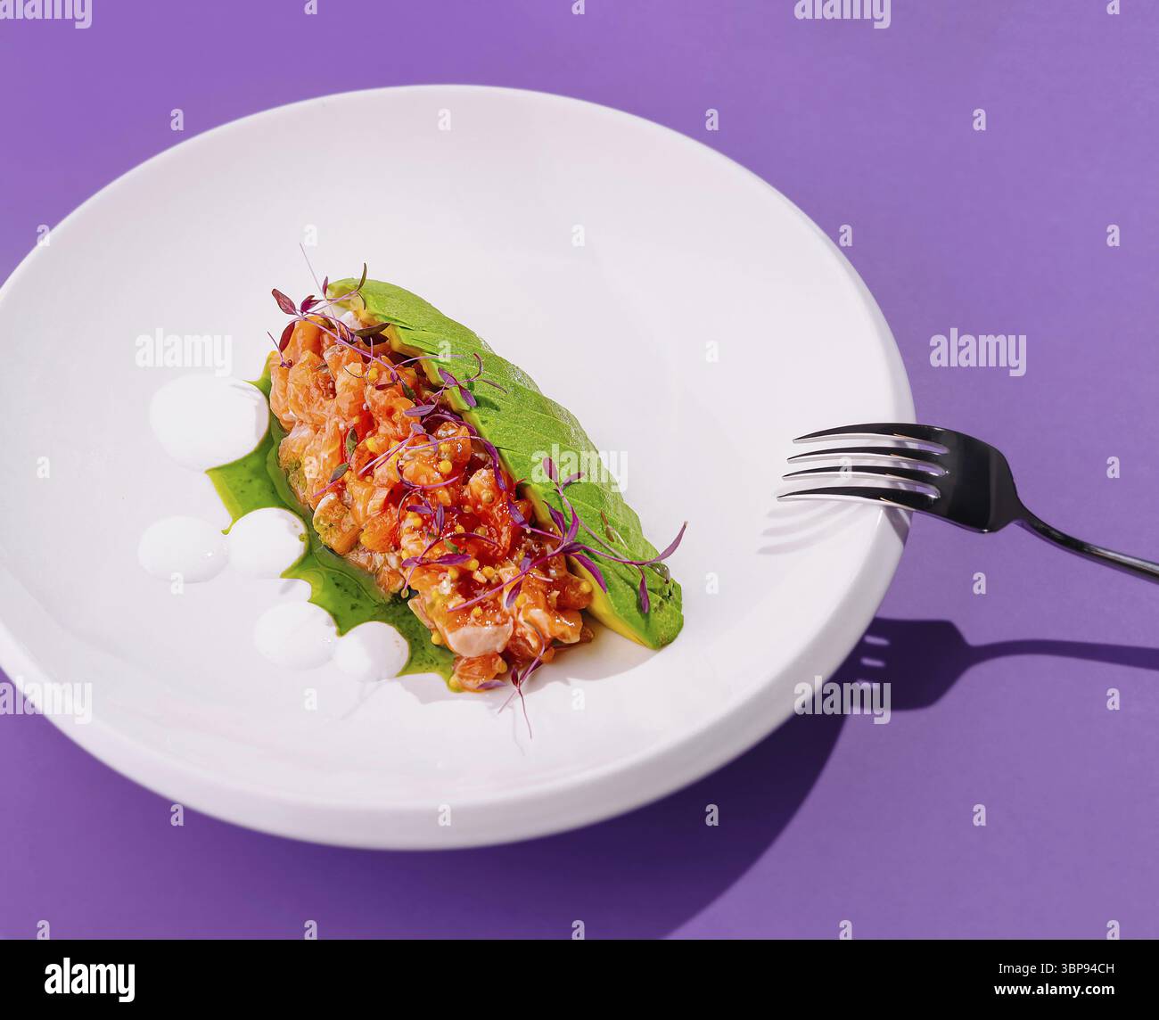 Cibo, antipasto alla tartare di salmone servito con avocado con microverdure e salsa su piatto bianco su sfondo viola Foto Stock