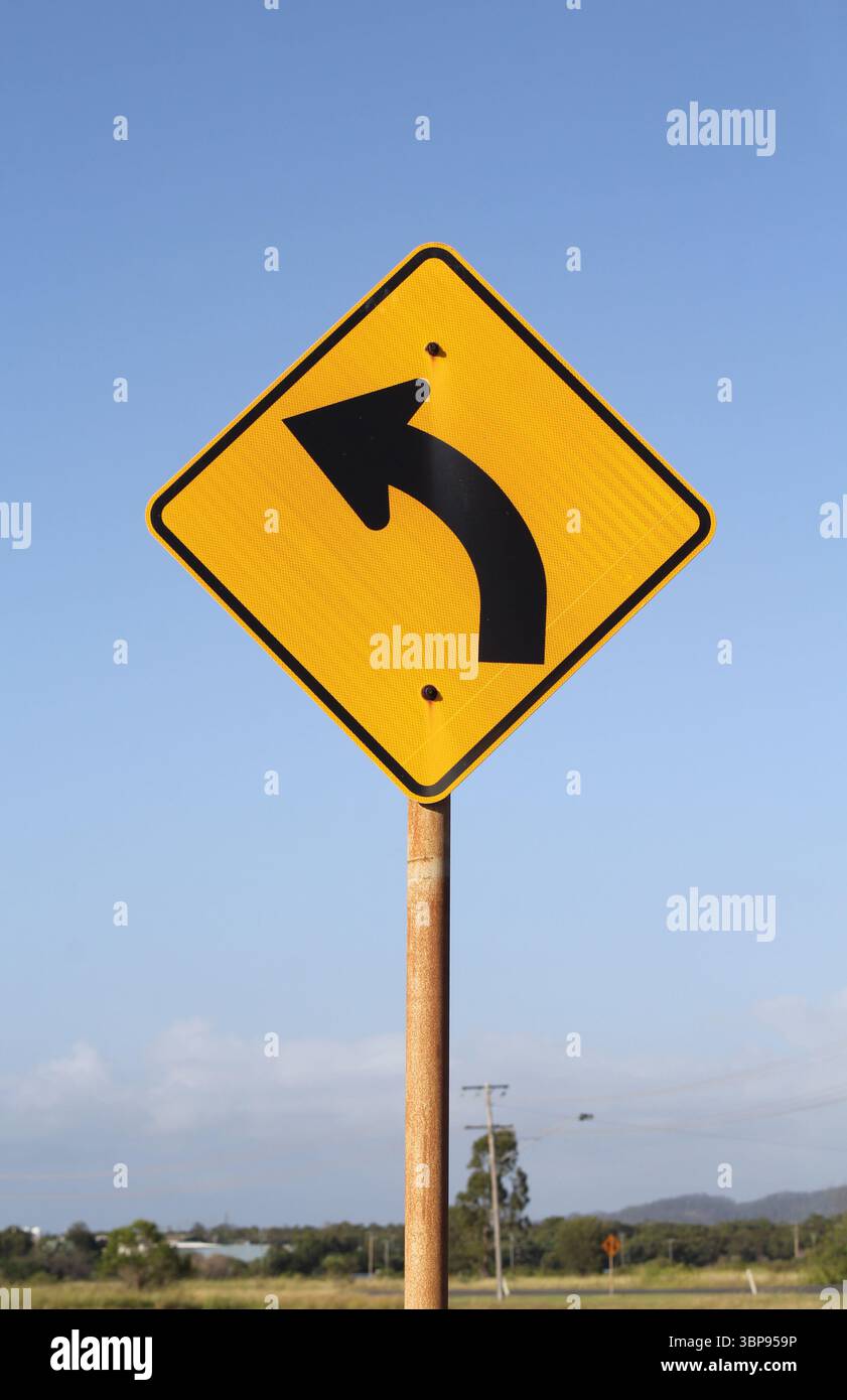 Cartello giallo a forma di diamante con la curva a sinistra contro un cielo azzurro Foto Stock
