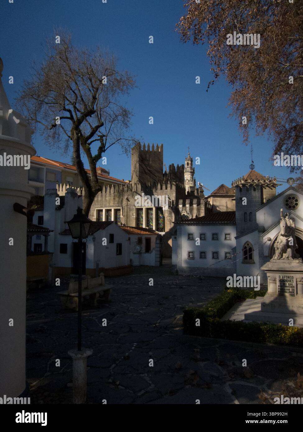 Una foto all'aperto di un cortile con una statua di D. Afonso Henriques, il primo re del Portogallo. Il cortile è circondato da piccoli edifici bianchi Foto Stock