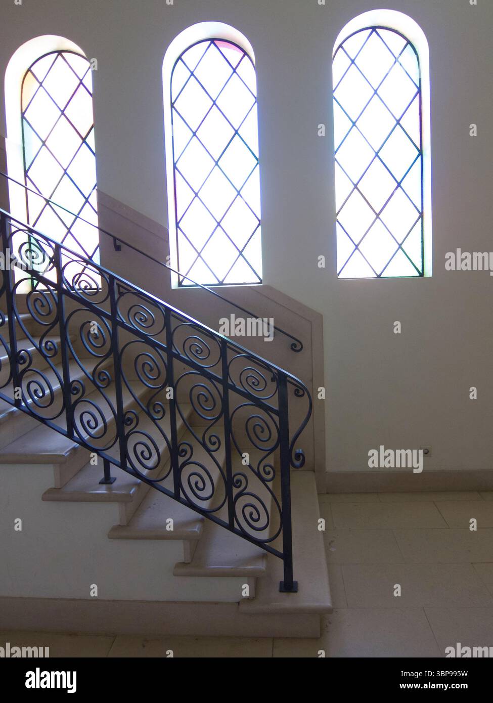 Una scala con una ringhiera decorativa in ferro battuto e tre finestre ad arco con pannelli a diamante. Foto Stock
