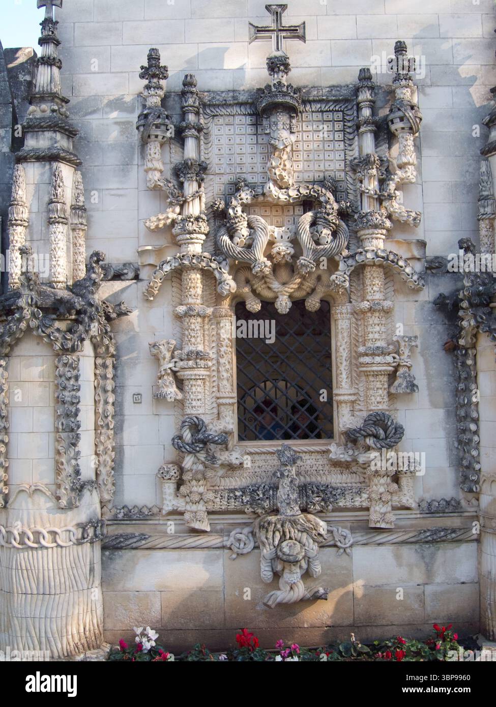 Una vista dettagliata di una finestra ornata su un edificio in pietra, caratterizzato da intricate incisioni e una croce in cima. Foto Stock