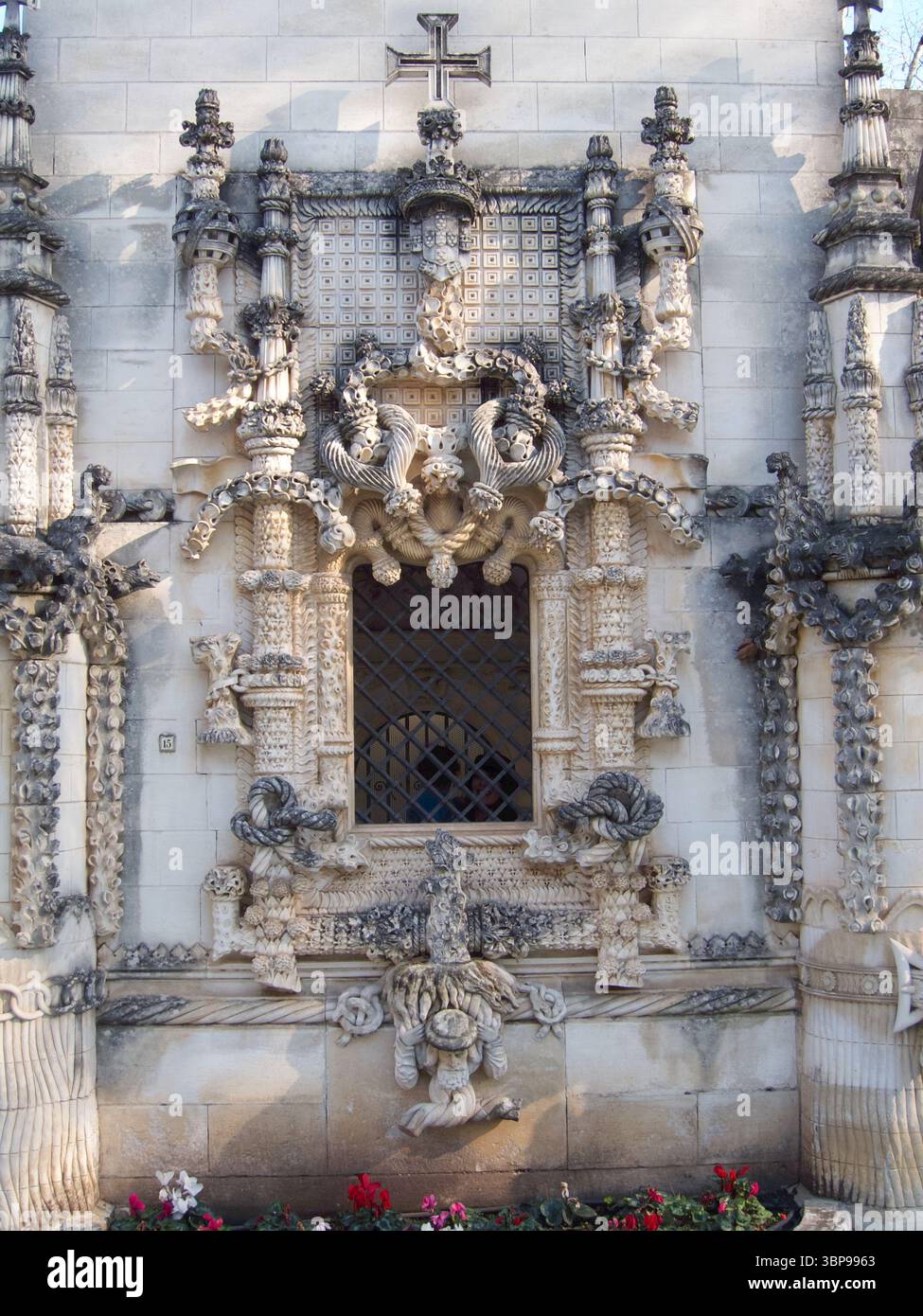 Una vista dettagliata di una finestra ornata su un edificio in pietra, caratterizzato da intricate incisioni e una croce in cima. Foto Stock