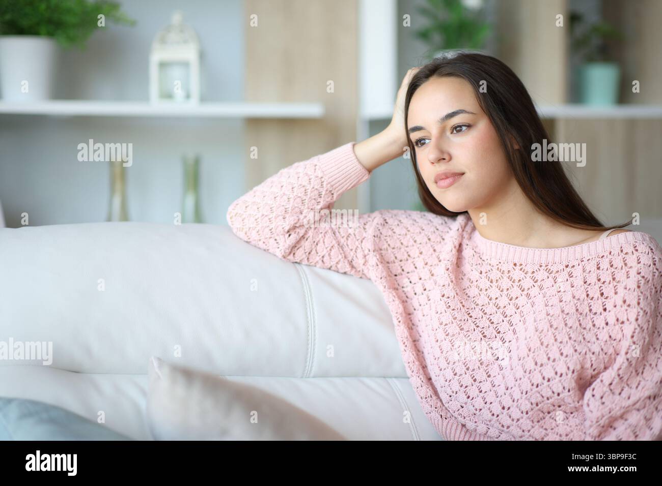 Una donna in salotto guarda lontano seduto su un divano di casa Foto Stock