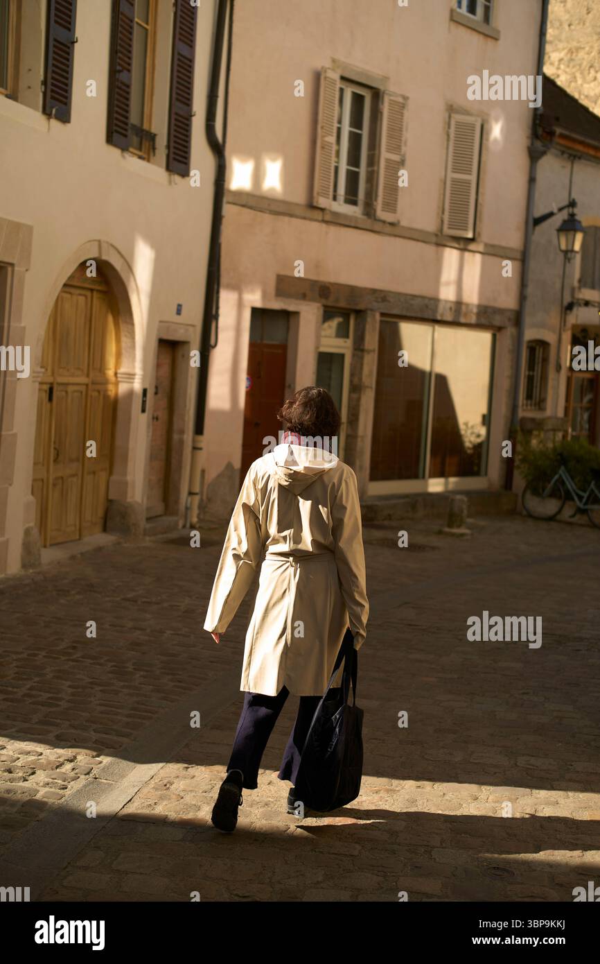 Donna in un trench che cammina su una strada acciottolata in una città europea. Borgogna, Francia Foto Stock