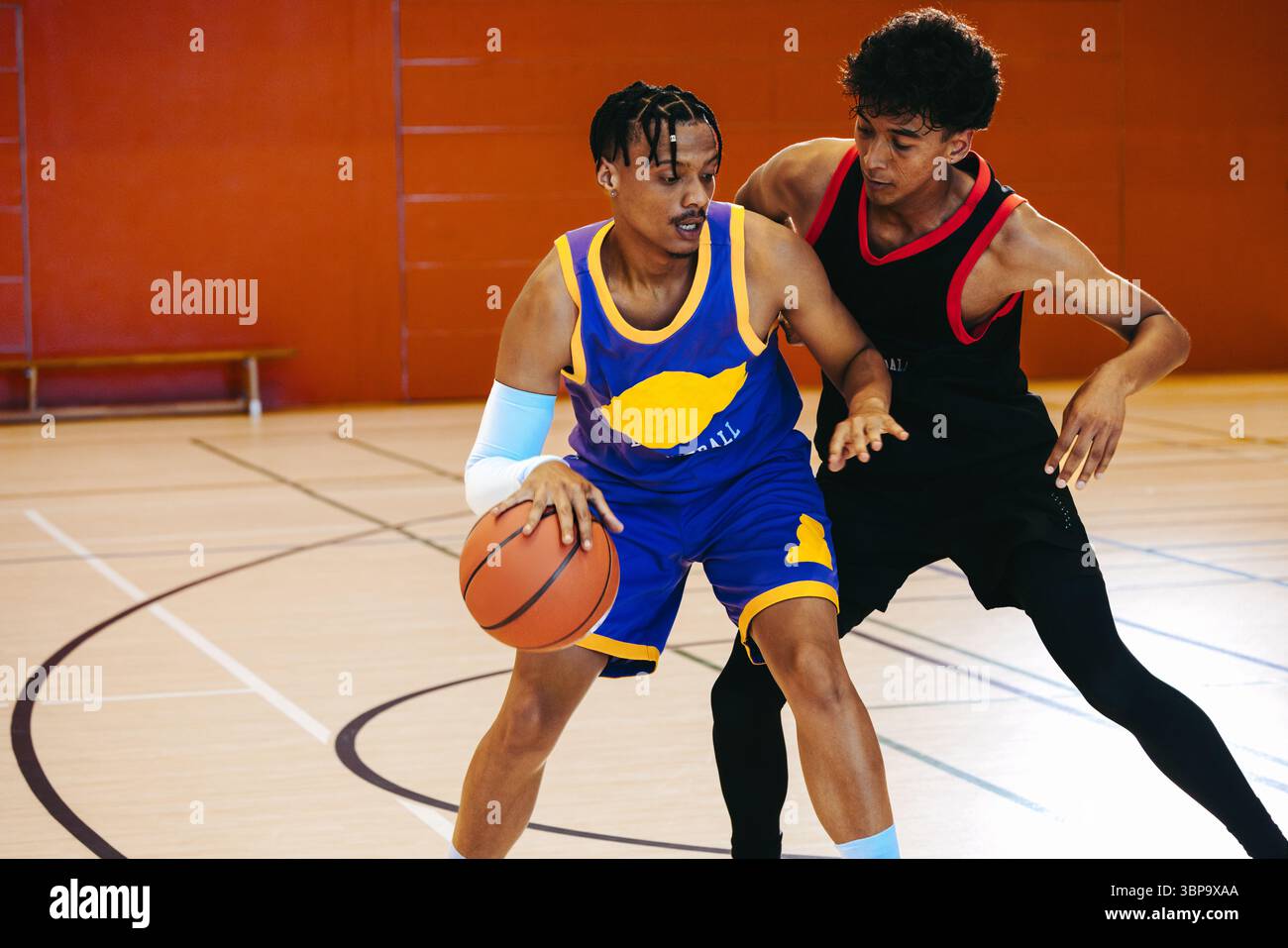 Un giovane giocatore maschile di basket dribbla con uno scopo, affrontando un difensore in una partita tesa uno contro uno. Foto Stock