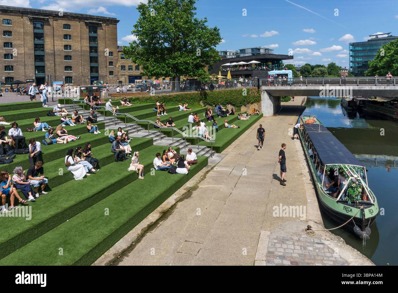 Persone sedute accanto al Regent's Canal in Granary Square, King's Cross. Foto Stock