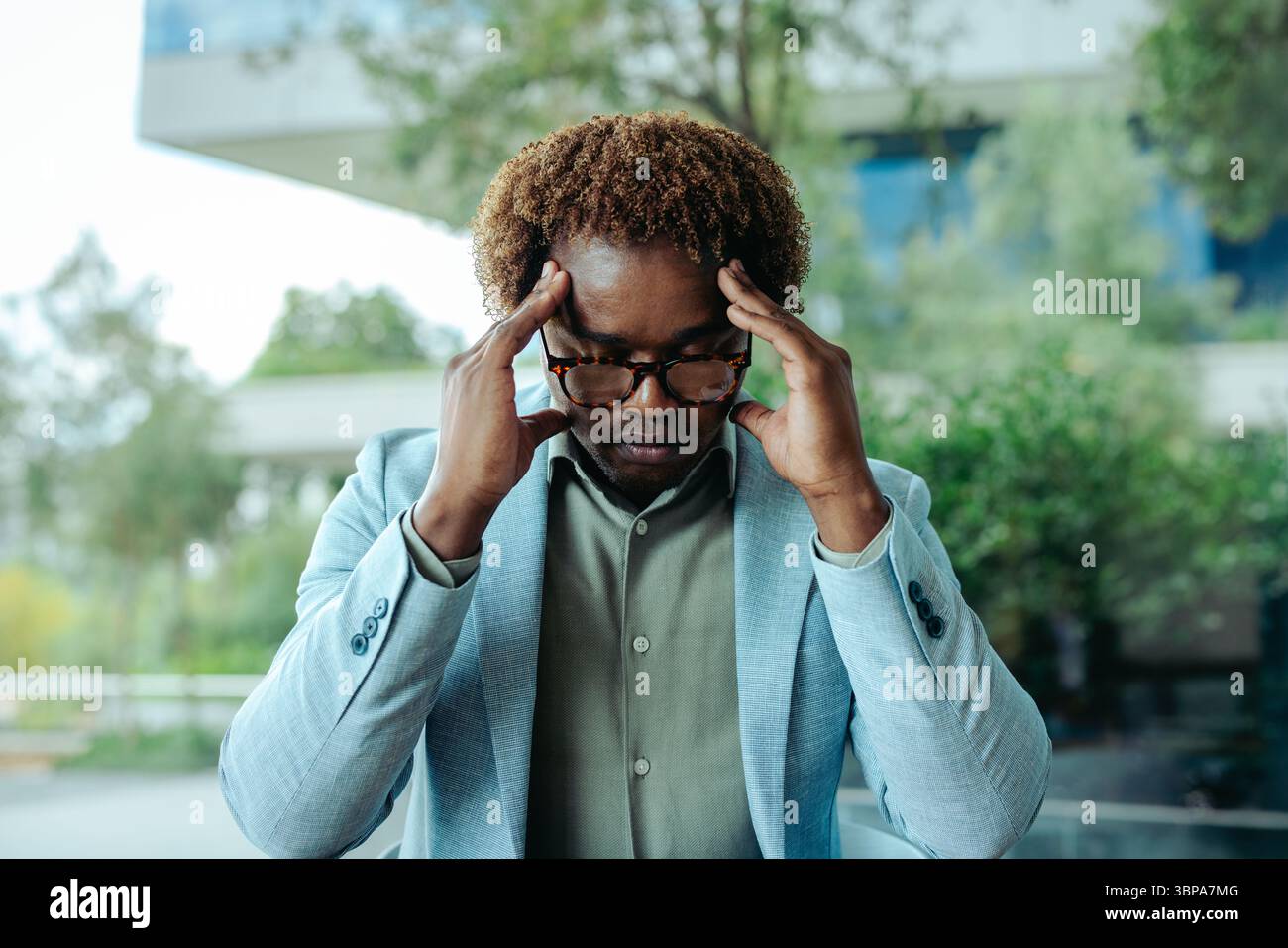 Un professionista maschile sembra preoccupato e stressato mentre si trova in un ufficio moderno. Indossando un vestito, ha le dita sul suo tem Foto Stock