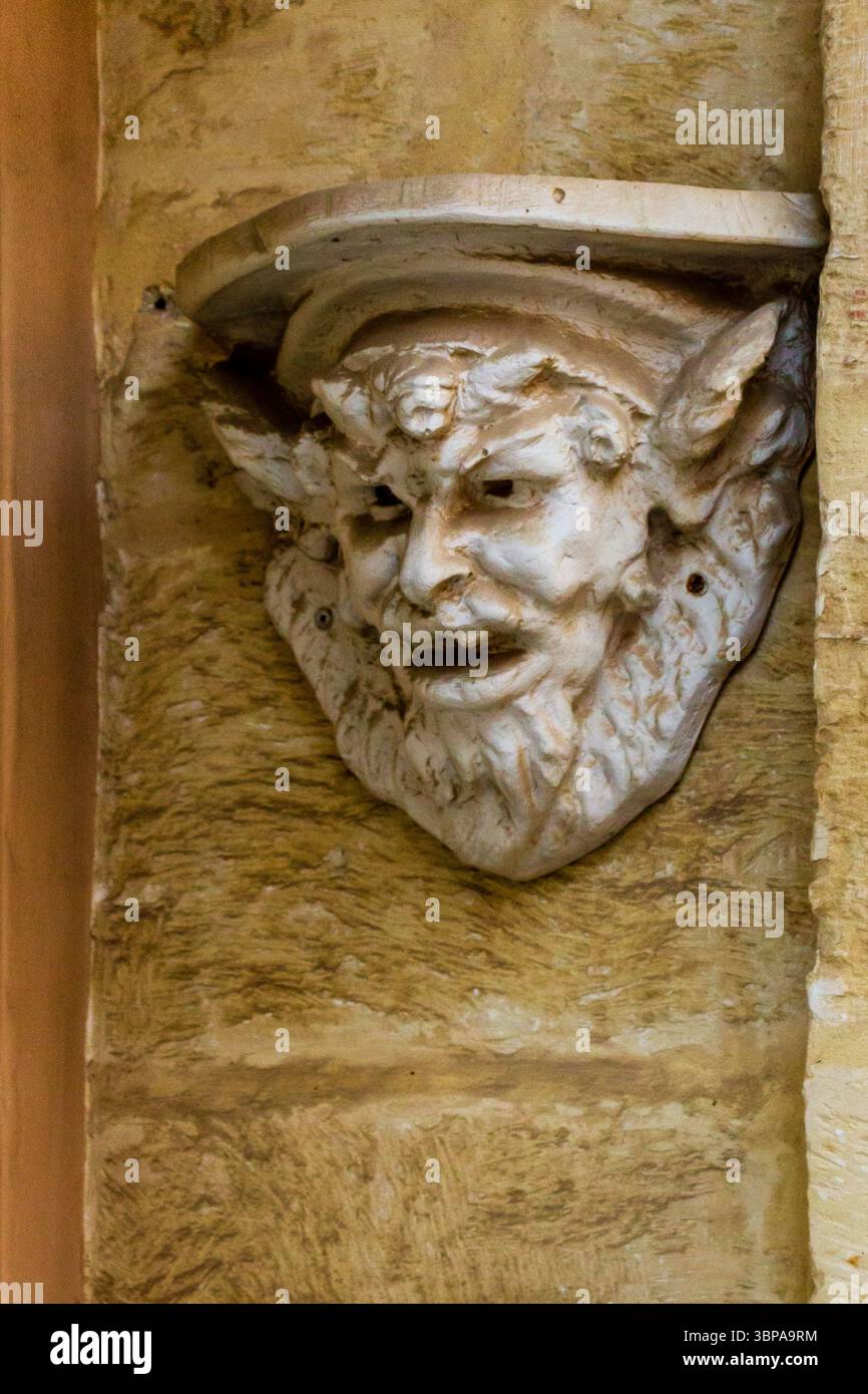 Scultura ornamentale in pietra di un volto mitico su un muro rustico Foto Stock