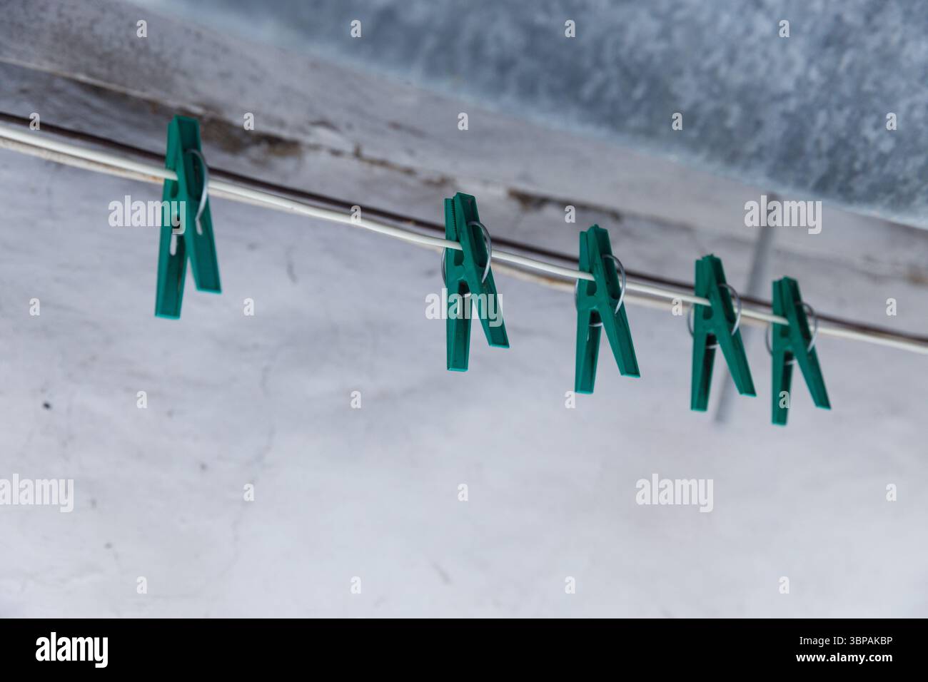 Primo piano di coloratissimi Clothespins verdi appesi su un filo metallico su uno sfondo morbido e testurizzato in un ambiente domestico Foto Stock
