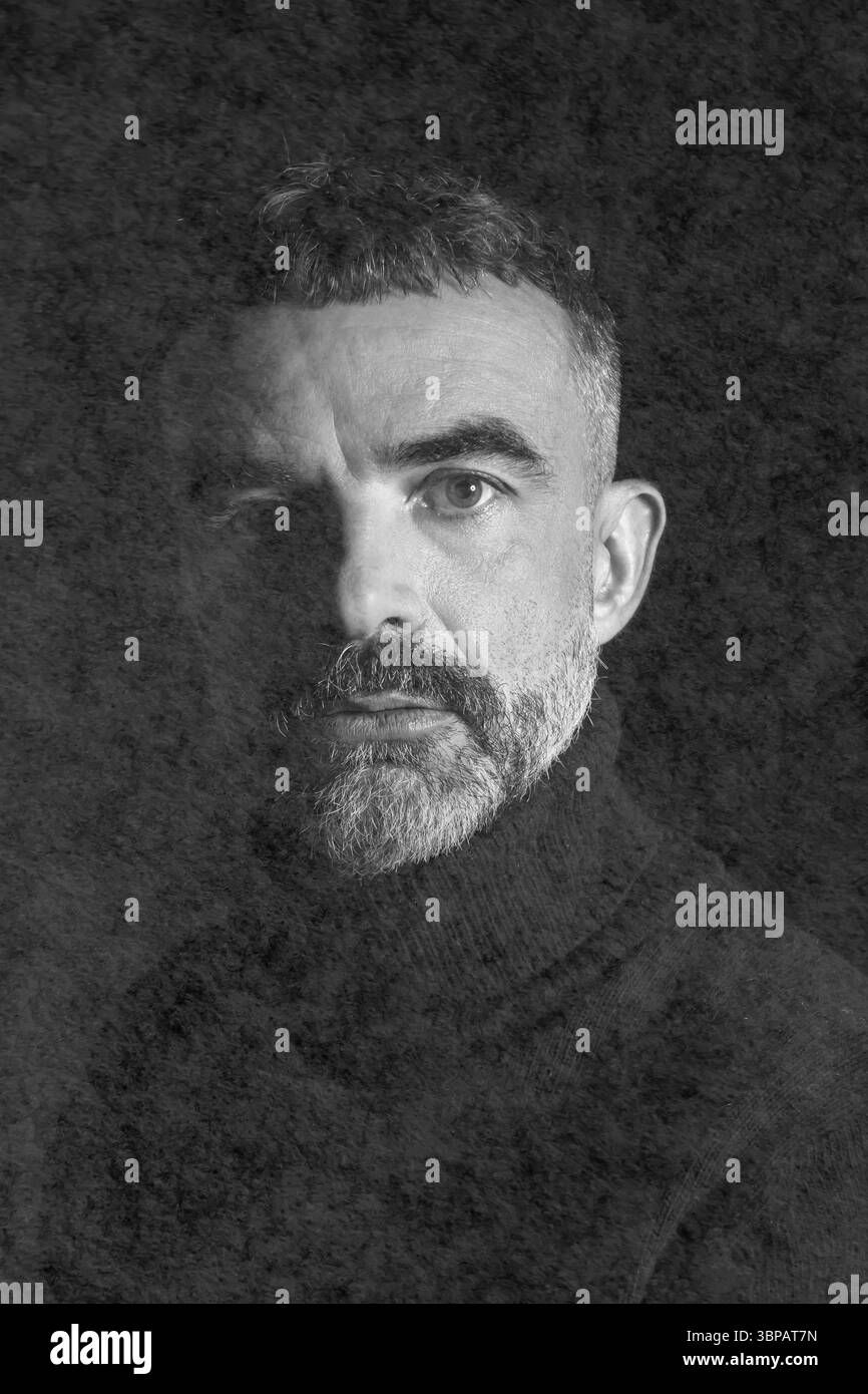 Moody ritratto in bianco e nero di un uomo barbuto maturo con capelli corti, che indossa un dolcevita scuro, parzialmente illuminato da un'ombra drammatica. Foto Stock