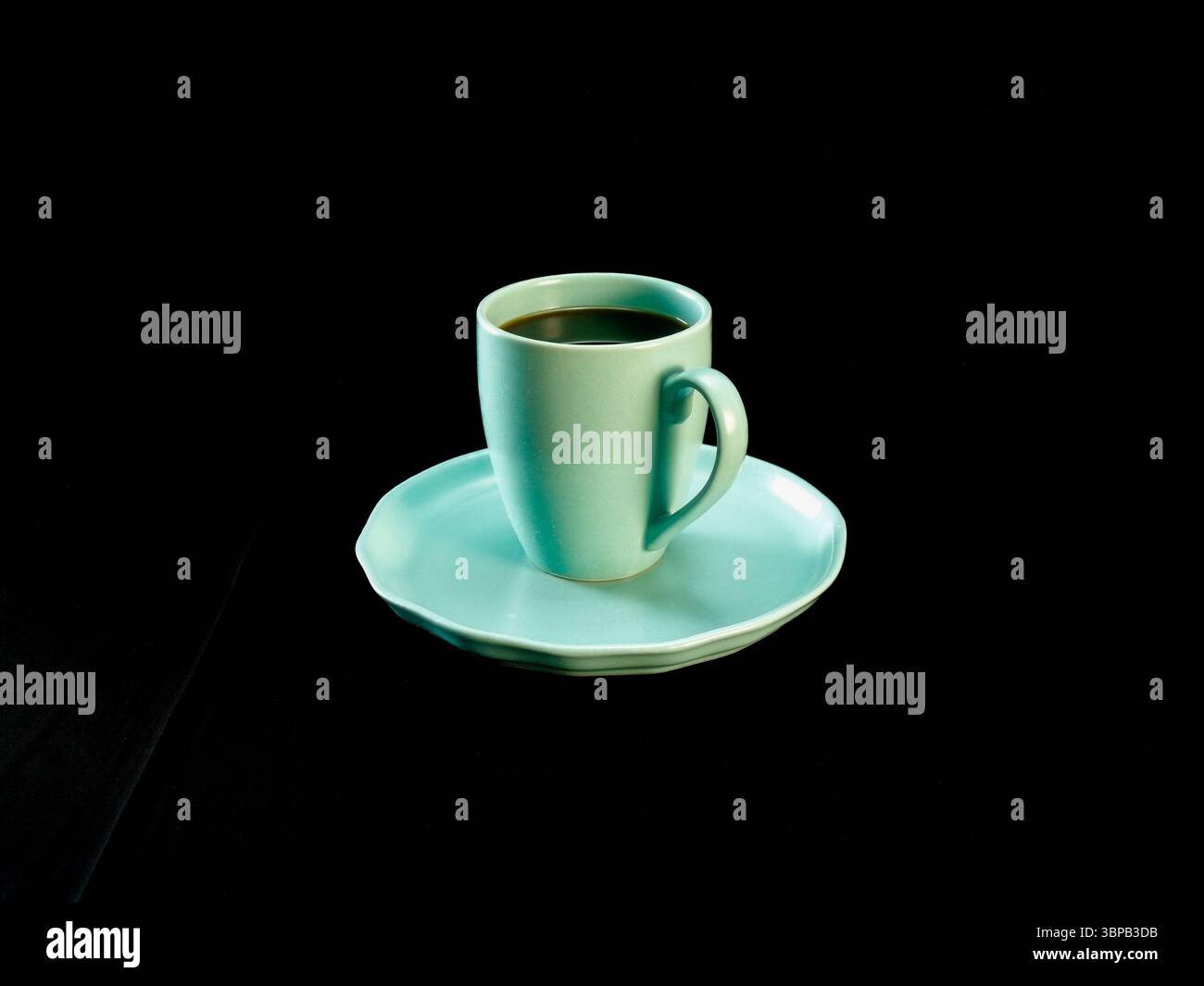 Foto minimalista di una tazza di caffè verde menta su un piattino coordinato, posizionata su uno sfondo nero in tessuto. Ideale per concetti relativi al mattino Foto Stock