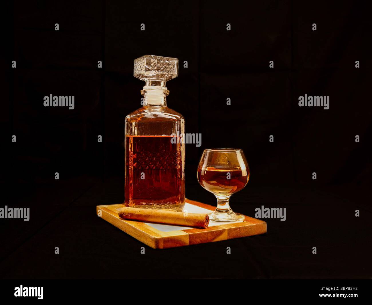 Elegante decanter per whisky e bicchiere servito su un vassoio di legno con un sigaro arrotolato, su sfondo scuro Foto Stock