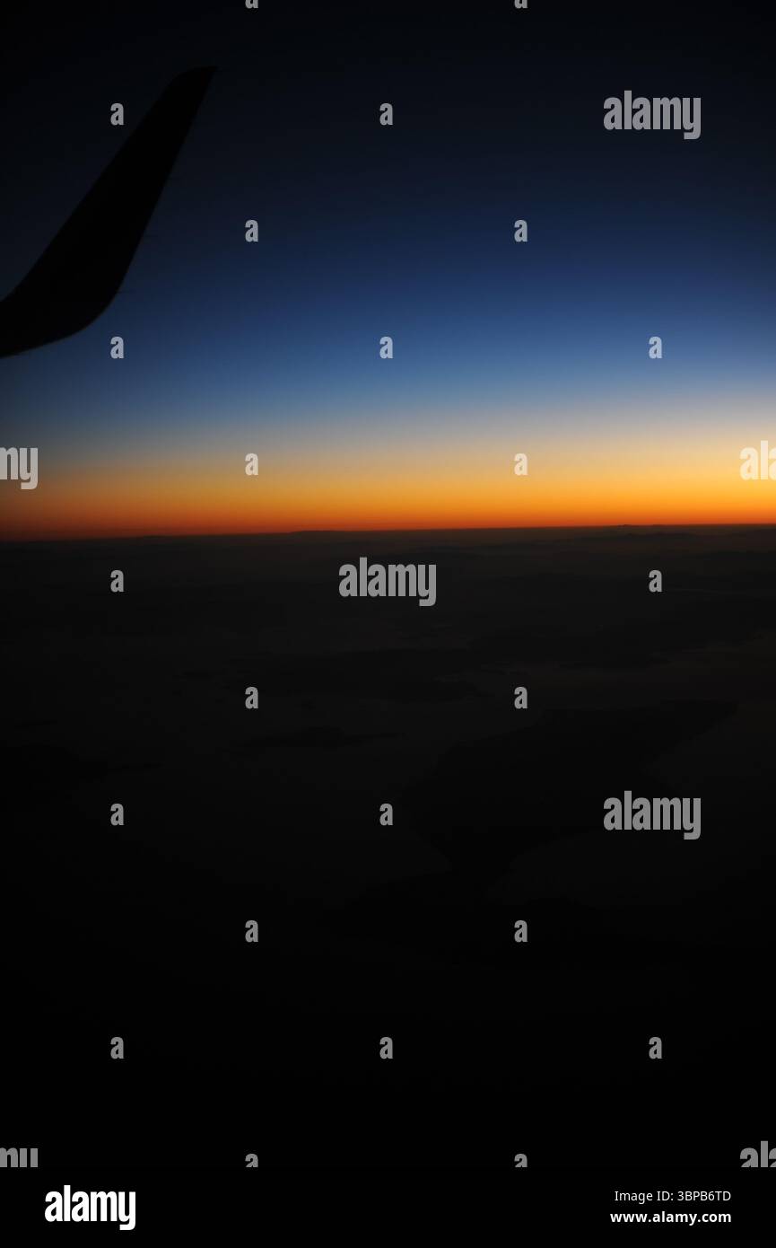 Ala dell'aeroplano durante il volo in aria sopra le nuvole al crepuscolo e all'alba prima dell'alba con cielo limpido con orizzonte limpido in estate Foto Stock