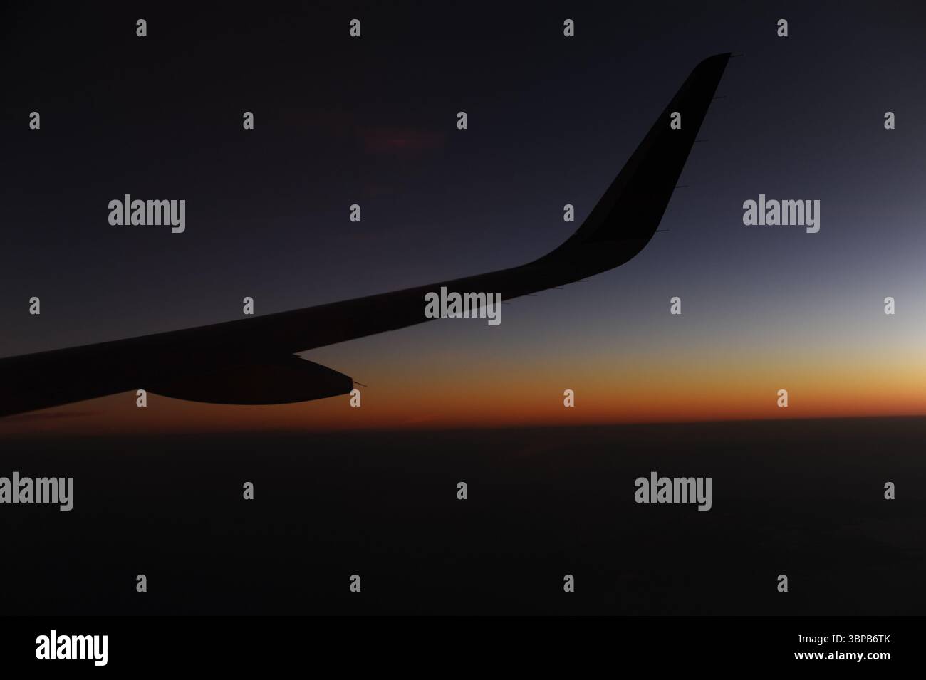 Ala dell'aeroplano durante il volo in aria sopra le nuvole al crepuscolo e all'alba prima dell'alba con cielo limpido con orizzonte limpido in estate Foto Stock