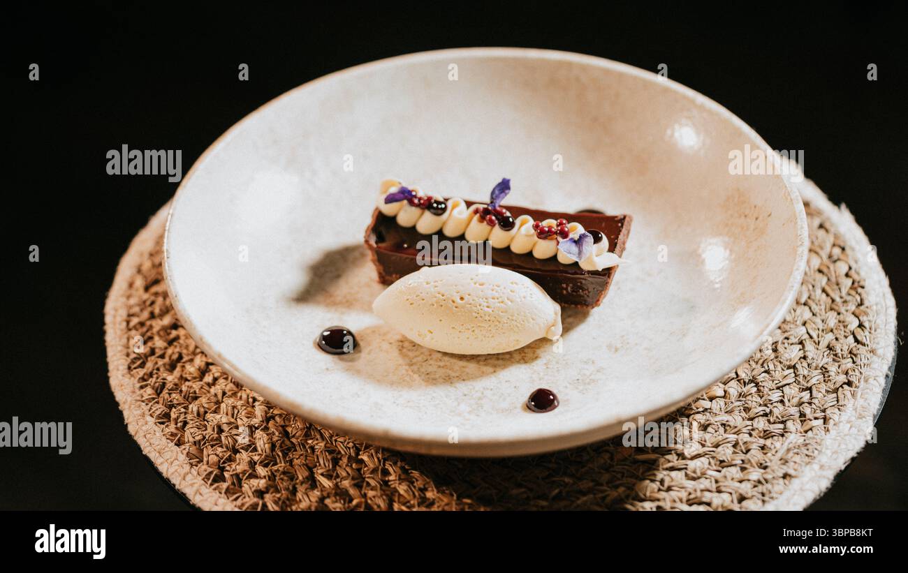 Un dessert con base bianca e una copertura marrone scuro. Il dessert è servito su un piatto bianco con bordo nero Foto Stock