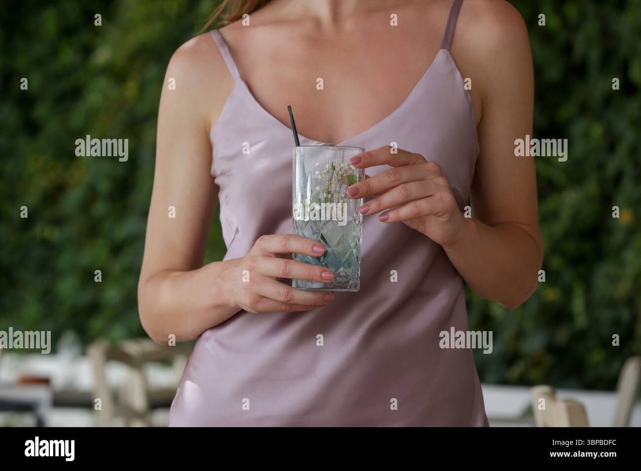 Elegante donna in abito camisole di seta con un bicchiere di cocktail mojito appena preparato e godendosi una tranquilla giornata estiva Foto Stock