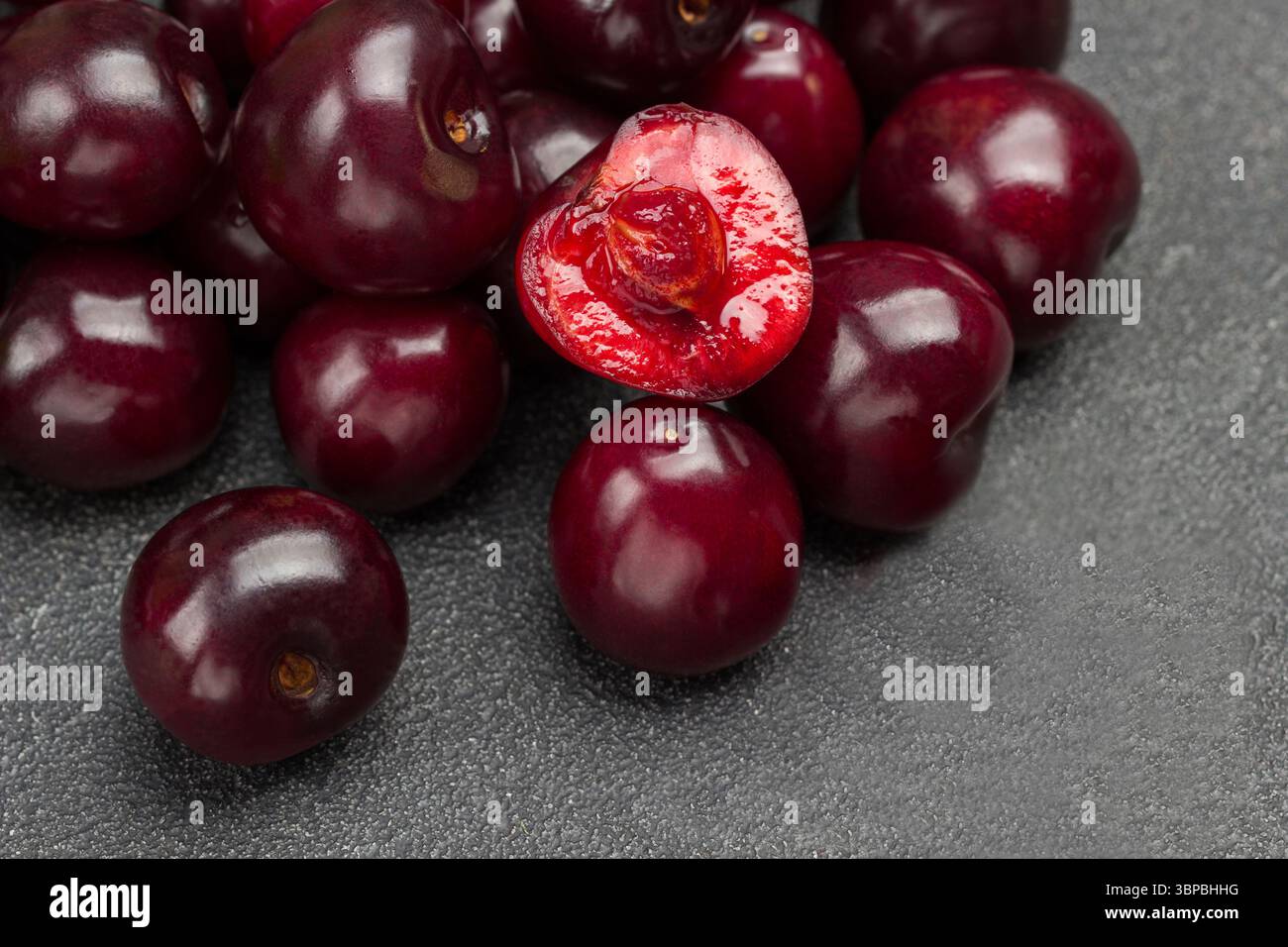Un mucchio di ciliegie mature. Mezza ciliegia, polpa e noccioli di ciliegia. Primo piano. Sfondo nero. Vista dall'alto. Foto Stock