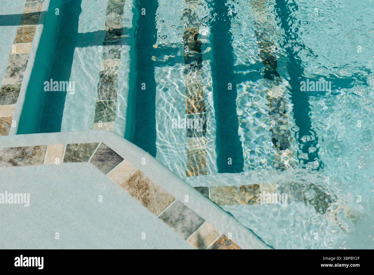 L'acqua increspata dolcemente in una piscina, mostrando splendidi disegni di piastrelle sotto la luce del sole. Foto Stock