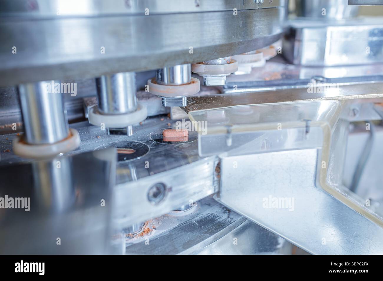 Primo piano di apparecchiature automatizzate per la produzione di compresse farmaceutiche in una struttura sterile, evidenziando la moderna produzione di farmaci Foto Stock