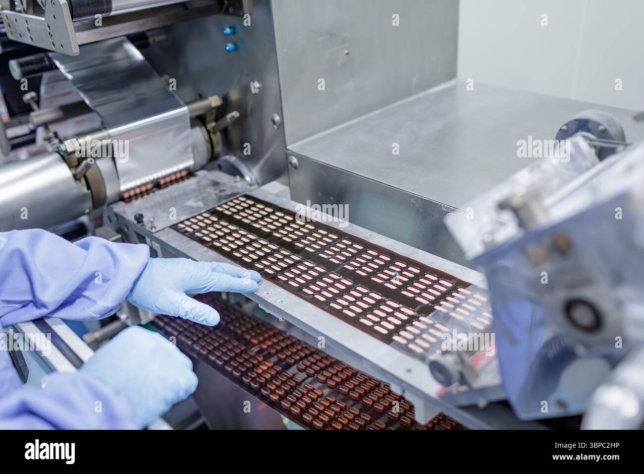 Confezionamento automatizzato in blister di compresse su una moderna linea di produzione farmaceutica con tecnici in ambiente sterile Foto Stock