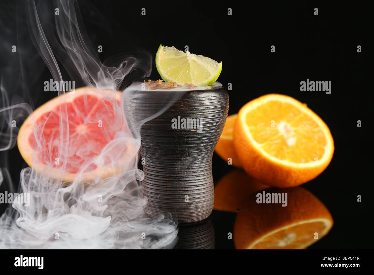 Ciotola di narghilè con fumo e frutta sul tavolo nero, primo piano Foto Stock