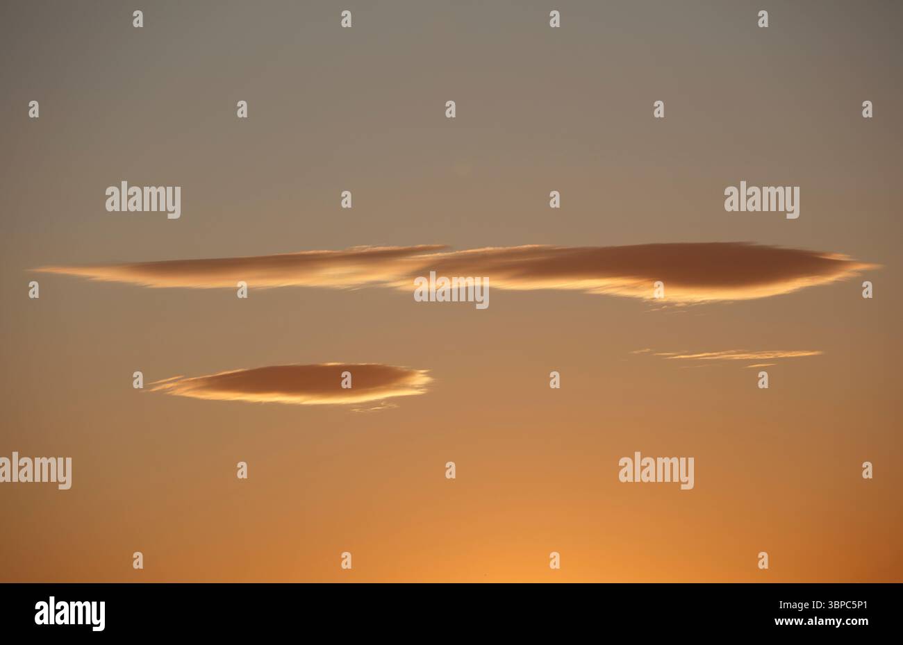 Sereno cielo artistico al tramonto, morbide nuvole allungate che riflettono un delicato bagliore dal tranquillo e tranquillo tramonto del sole, calde sfumature arancioni gialle Foto Stock