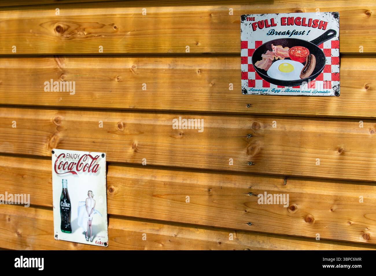 Parete in legno con cartelli in metallo retrò che pubblicizzano una colazione all'inglese completa e Coca-Cola con un design vintage Foto Stock