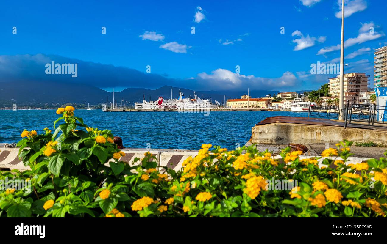 Traghetto operato da Toremar nel porto in attesa di passeggeri. In primo piano - fiori gialli e mare blu. 28 settembre 2025. Piombino, Italia. Foto Stock