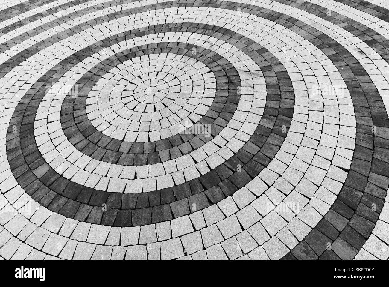 Vista ravvicinata astratta di uno schema di pavimentazione circolare costituito da pietre chiare e scure alternate in monocromia. La ripetizione geometrica crea un visu Foto Stock