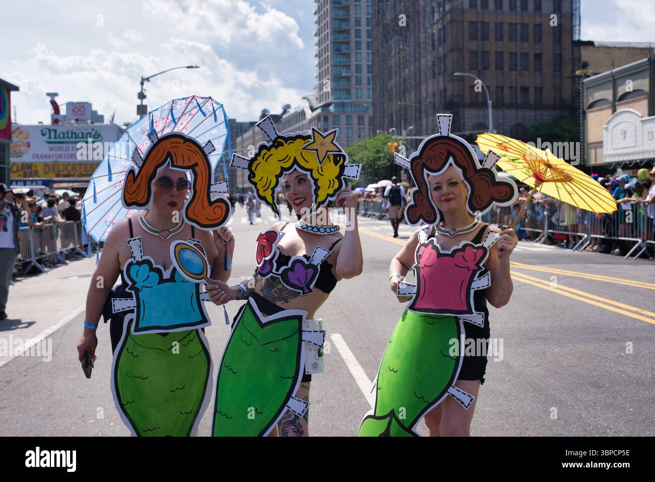 Tre donne in costumi a tema sirena partecipano a una sfilata di strada. Ogni costume presenta un grande ritaglio di carta con parrucca e corpetto stilizzati. Loro Foto Stock