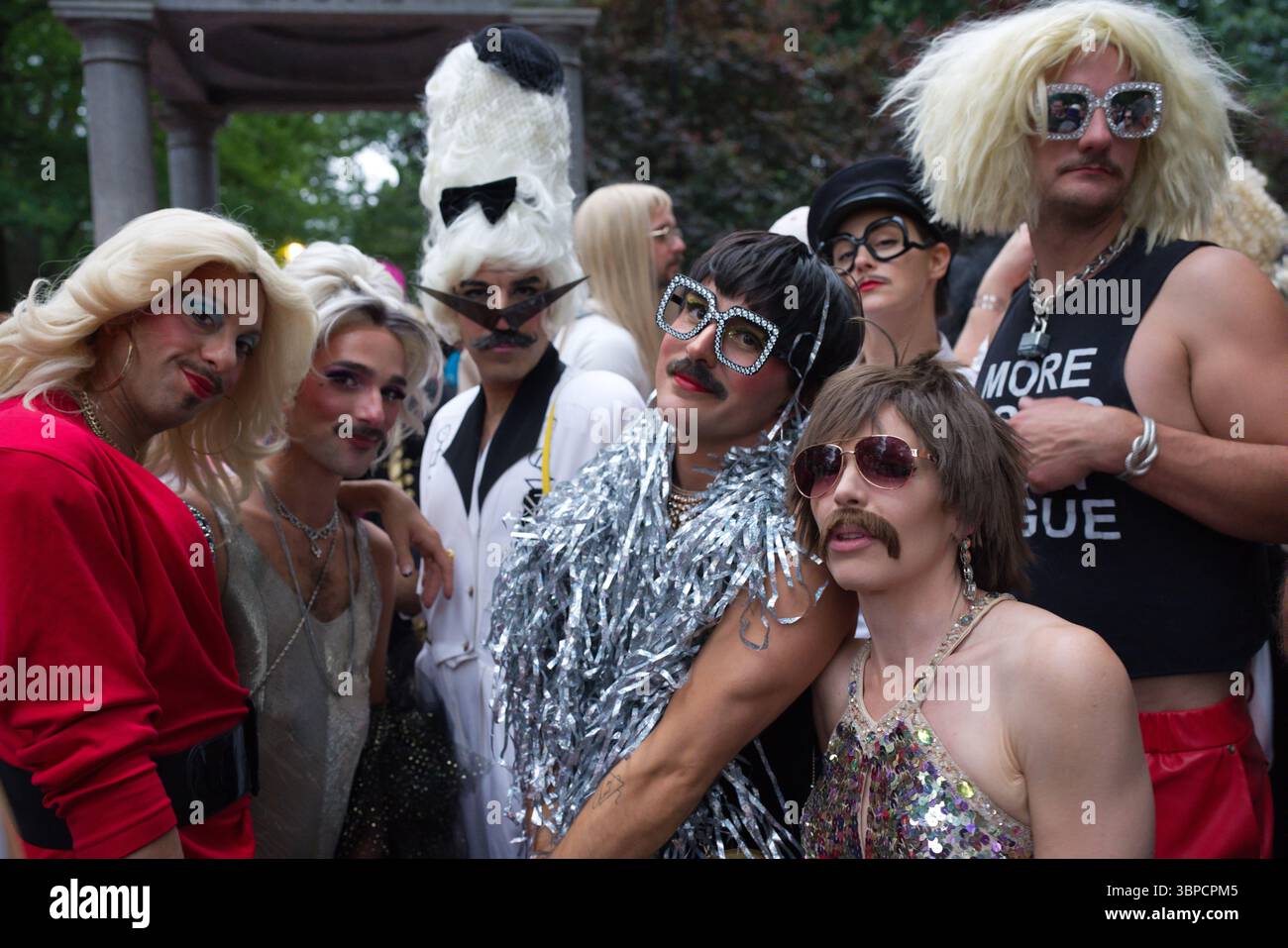 Un gruppo di individui in costumi e parrucche sgargianti, molti con occhiali da sole, sono riuniti da vicino. La scena è all'aperto, con bac disattivato Foto Stock