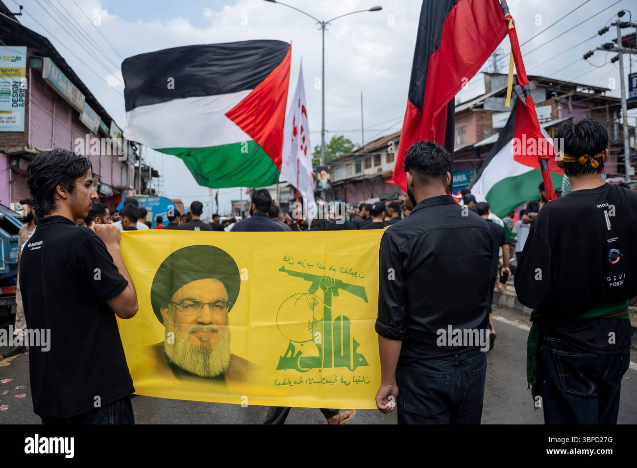 I musulmani sciiti del Kashmir detengono una bandiera del capo assassinato di Hezbollah, Sayyed Hassan Nasrallah, e una bandiera di Hezbollah, mentre un protestatore sventola una bandiera palestinese sullo sfondo durante l'undicesimo giorno della processione di Muharram. Migliaia di sciiti in lutto hanno partecipato alle processioni di Muharram per commemorare il martirio dell'Imam Hussain. Sabato, la polizia di Jammu e Kashmir ha registrato un caso contro diversi partecipanti per aver mostrato striscioni con il comandante di Hezbollah Hassan Nasrallah durante la processione.tra le tensioni aumentate a seguito del conflitto Iran-USA, manifesti e striscioni raffiguranti Ira Foto Stock