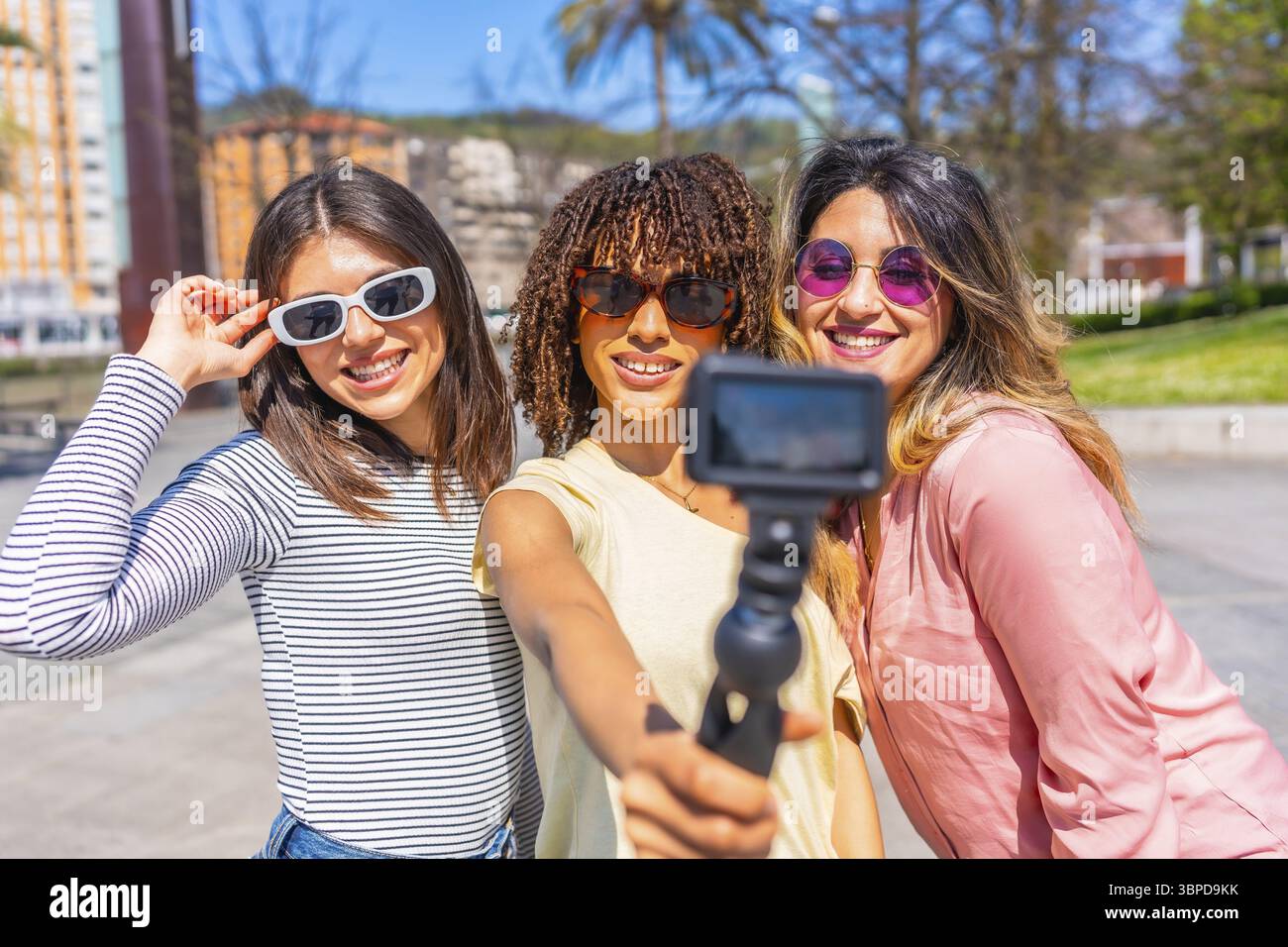 Donne multietniche che si godono le vacanze estive in città, utilizzano la fotocamera per filmare se stesse, catturando momenti di gioia e ricordi insieme Foto Stock
