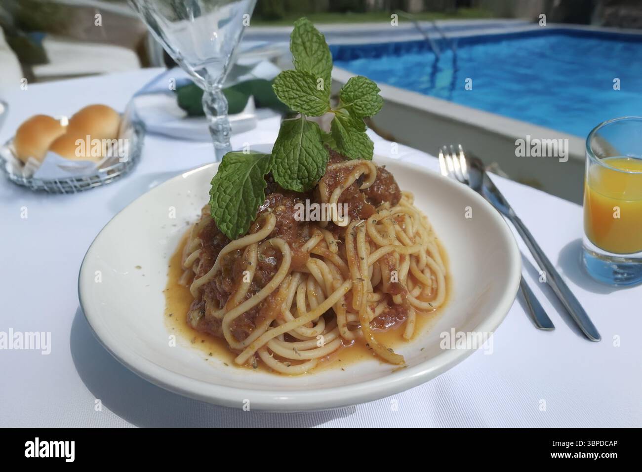 spaghetti con polpette serviti su un rustico tavolo di legno su una soleggiata terrazza a bordo piscina. Goditi un pasto perfetto all'aperto con una vista rinfrescante. Questo vi Foto Stock