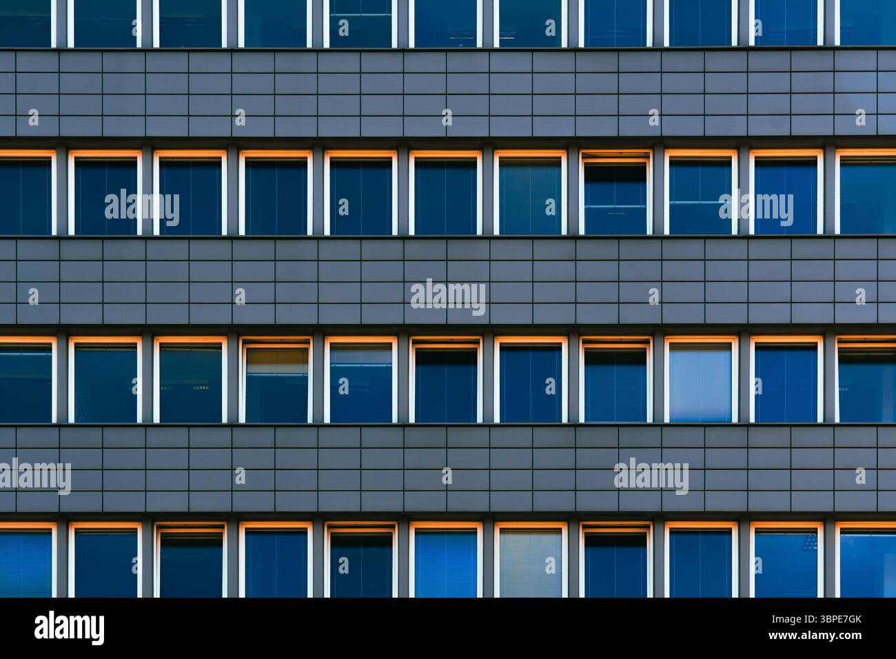 Facciata simmetrica di un edificio di uffici con finestre ripetitive e caldi accenti di luce solare Foto Stock