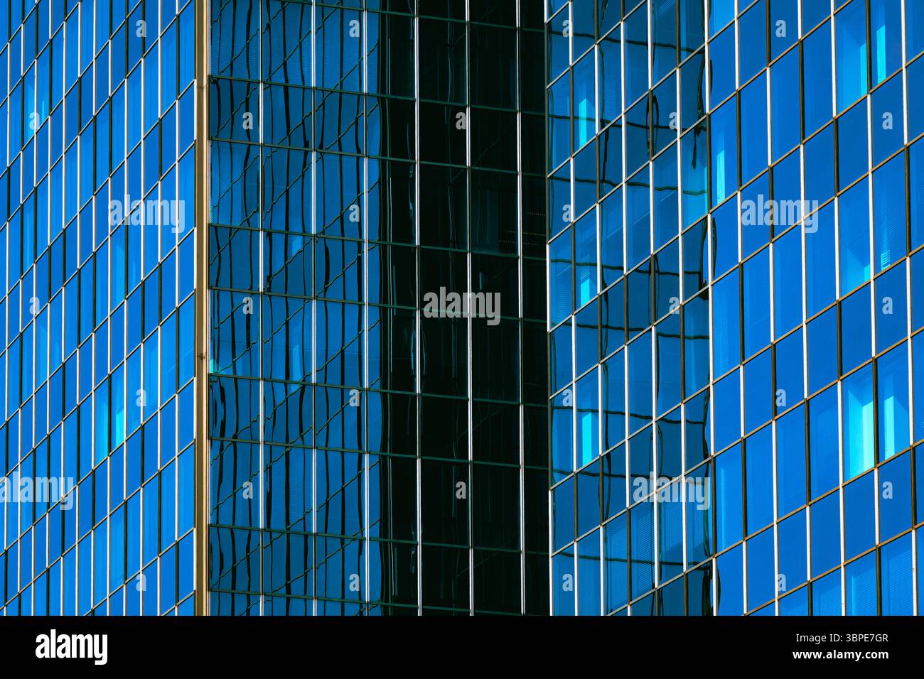 Facciata riflettente in vetro blu con strisce verticali per finestre e riflessi nuvolosi Foto Stock