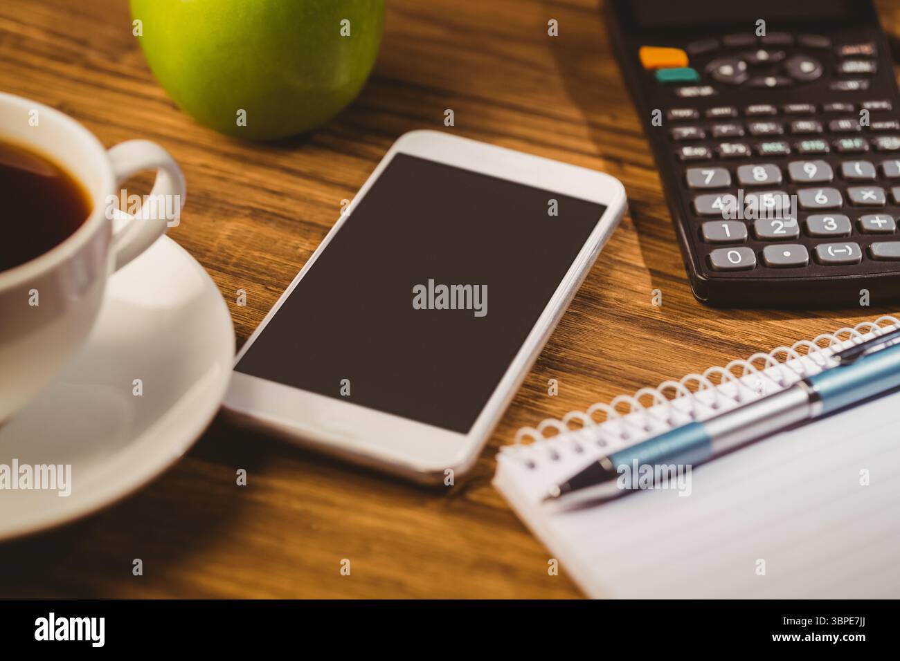 Il design piatto mostra la tazza di caffè, la mela, lo smartphone, la calcolatrice, il blocco note con penna su una scrivania in legno Foto Stock
