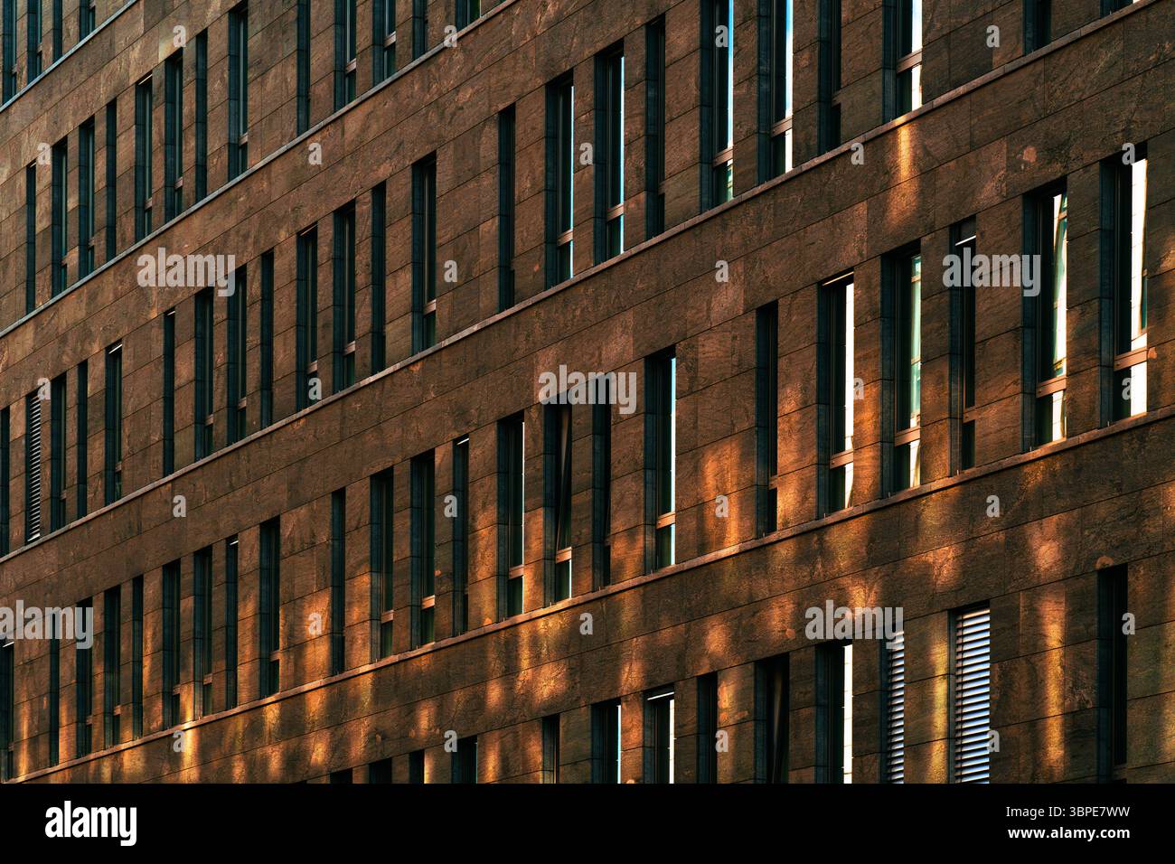 Facciata di un edificio moderno con finestre verticali ripetute illuminate dalla calda luce del sole, che creano forte contrasto geometrico e ritmo Foto Stock