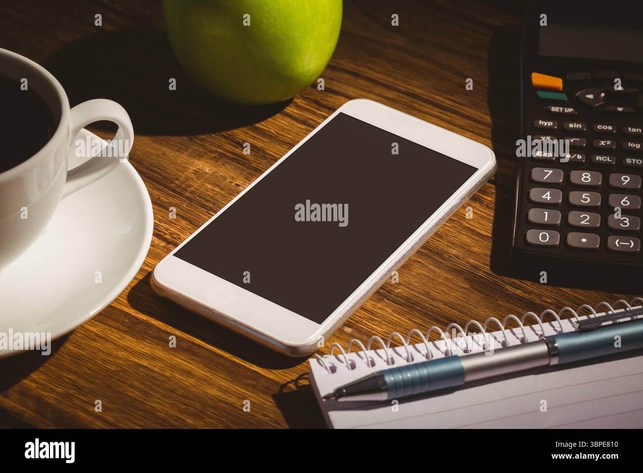 Design piatto che mostra lo smartphone sulla scrivania, la tazza di caffè e la mela verde, la calcolatrice, il notebook con penna Foto Stock